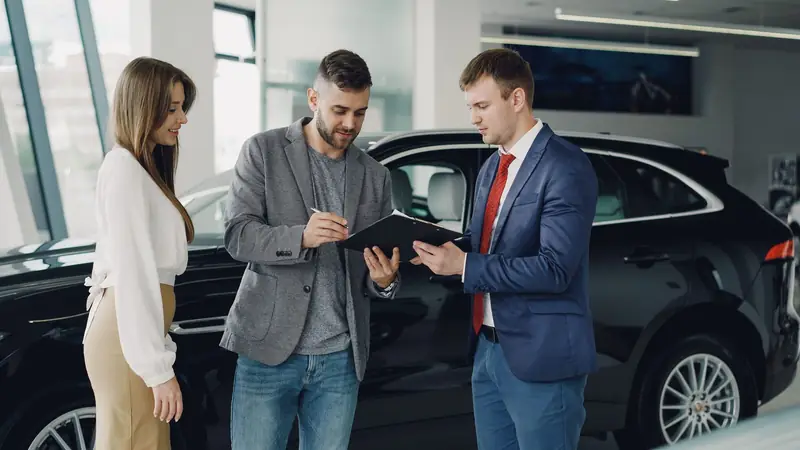 Casal fechando a compra de um carro com o vendedor na concessionária